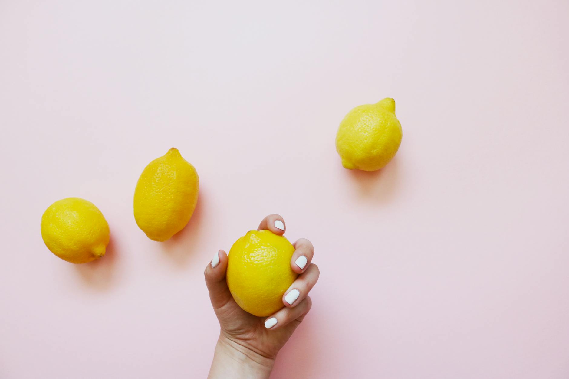 Hand holding a lemon on soft pink background, symbolizing desire and connection