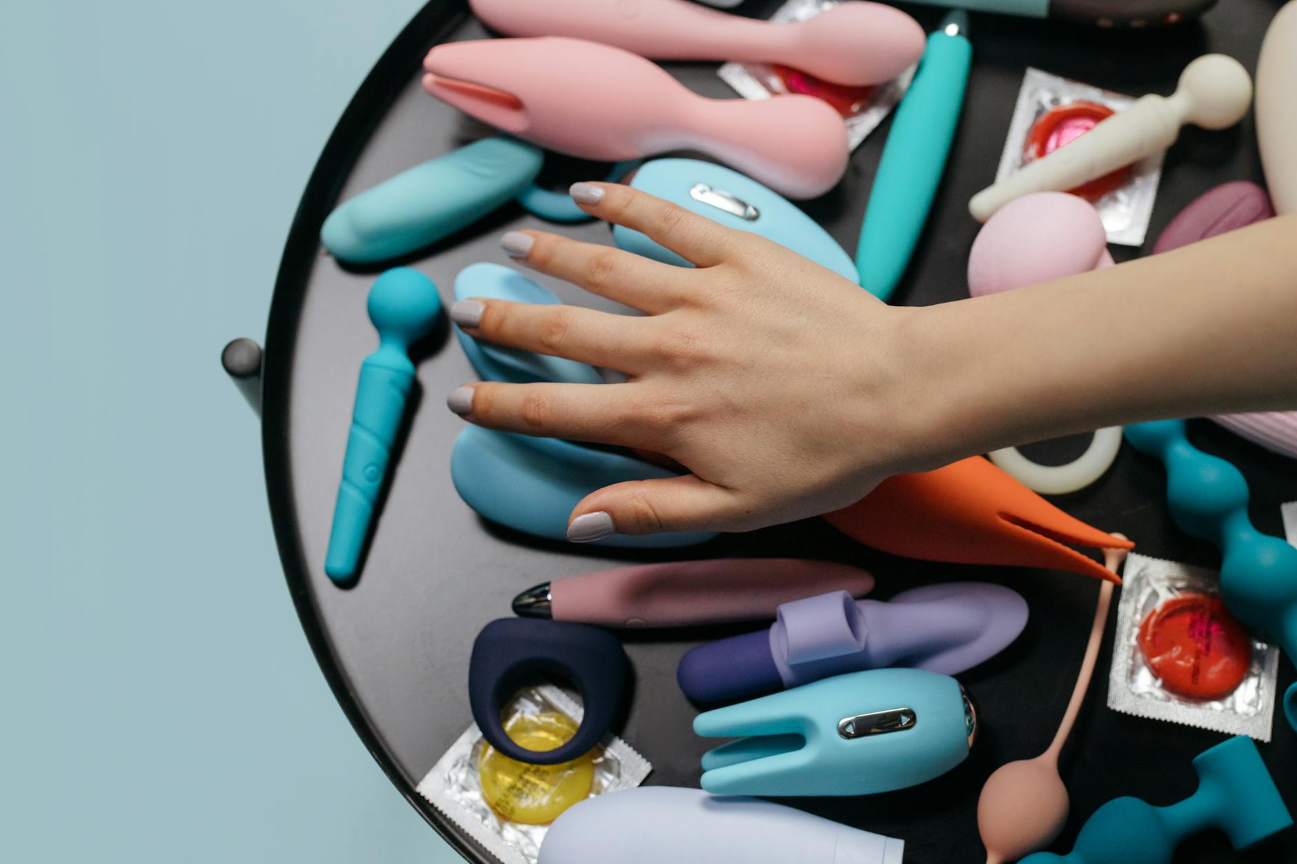 A hand selecting a vibrant lemon clitoral vibrator from a collection of adult toys on display