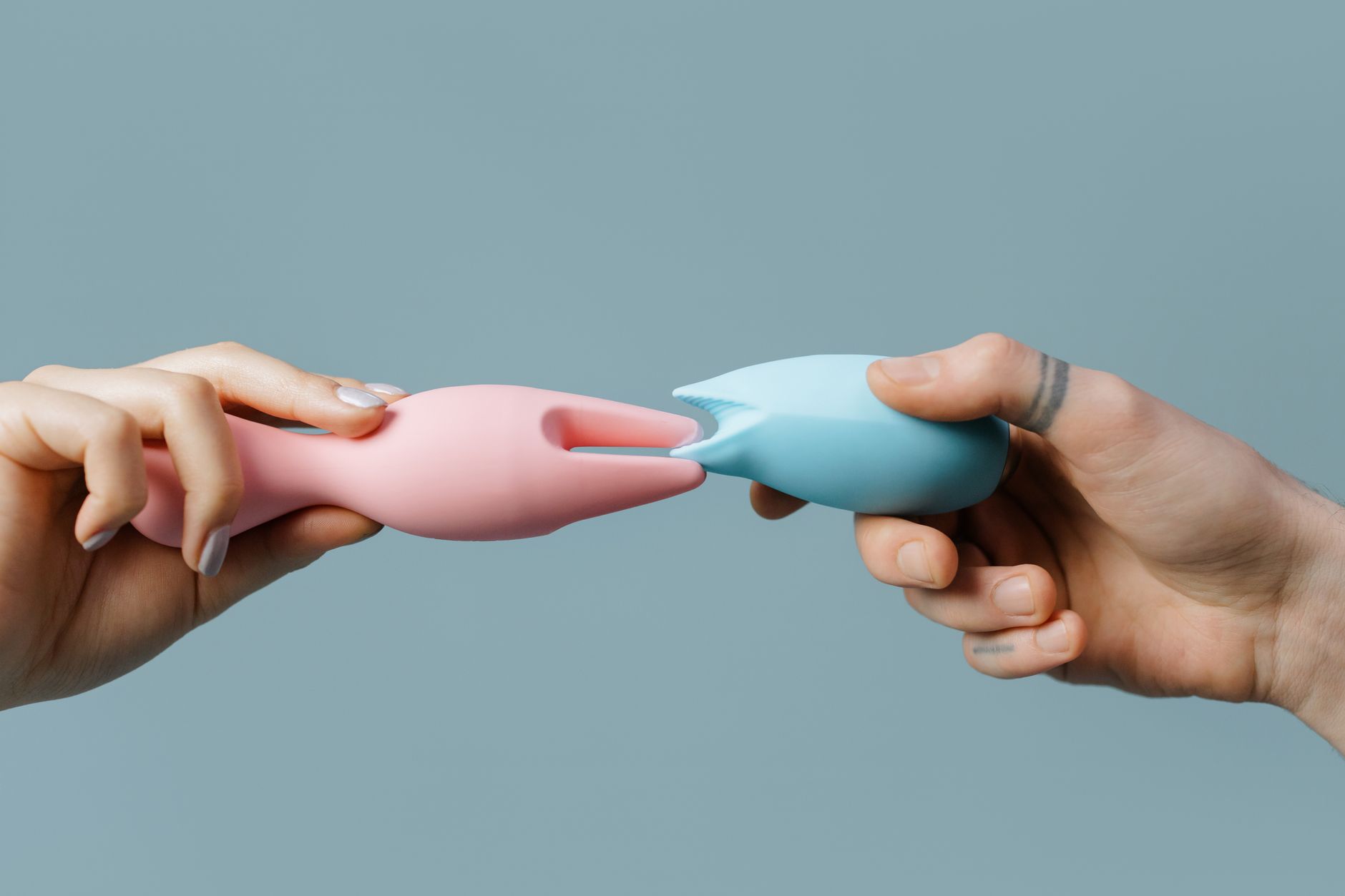 Hands holding silicone pleasure toys in soft pastel colors